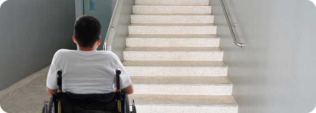 School building staircase, and a young student in a wheelchair looking at it.